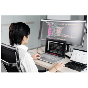 A SupremeX employee sits at a desk in a modern office, working on multiple screens displaying code and data. The setup includes a laptop, a large monitor, and a tablet, indicating a technical or IT-focused role.