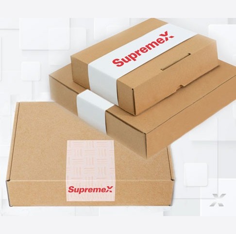 A set of brown corrugated packaging boxes with SupremeX branding, featuring both paperboard sleeves and labels. The top boxes are wrapped in custom white paperboard sleeves with the SupremeX logo, while the bottom box has a branded label affixed to the front. The background features a subtle geometric pattern, enhancing the clean and modern presentation of the packaging solutions.